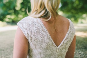 Close-up of a bride's back in a delicate lace dress, part of her London Hyde Park elopement photography session. Soft blonde hair drapes down, with a blurred green backdrop.