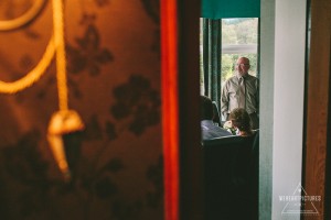 A celebrant speaks at Brittany and David's Isle of Skye Loch Coruisk humanistic wedding. Guests listen, framed by a doorway. "We Heart Pictures" logo visible.