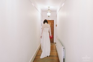 Bride walks down a hallway at Tewin Bury Farm, carrying a red clutch. The Tewin Bury Farm Wedding Photographer captured this moment of anticipation.