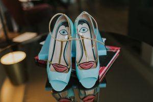 Unique light blue peep-toe heels with a quirky face design (eye and red lips) on the insole, resting on books. A creative detail captured by The Swan Shakespeare Globe Wedding Photographer.