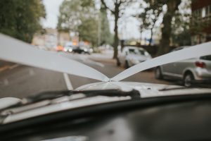 Close-up of white wedding ribbons on a car hood, taken by The Swan Shakespeare Globe Wedding Photographer. Street and other cars blurred in the background.