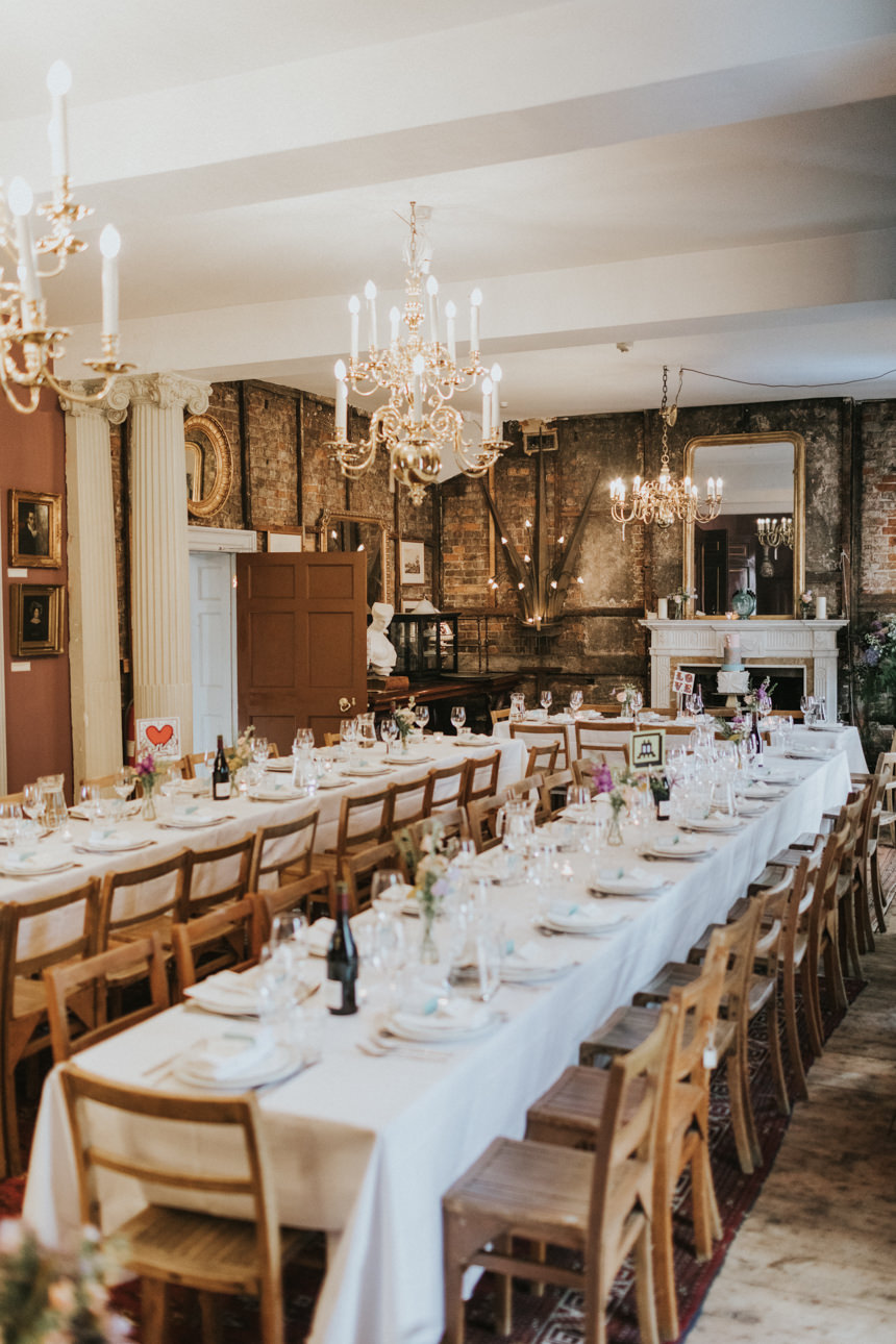 Brunswick House Wedding reception. Long tables are set with white linens, glassware, and flowers beneath vintage chandeliers, creating a warm, elegant atmosphere in the historic venue.