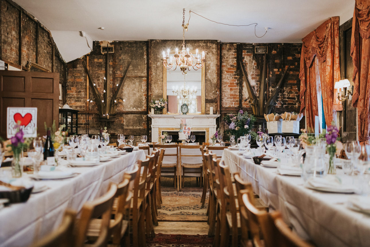 Brunswick House Wedding reception: Long tables set for a wedding feast, rustic exposed brick walls, chandelier, and vintage decor create a warm, intimate atmosphere.