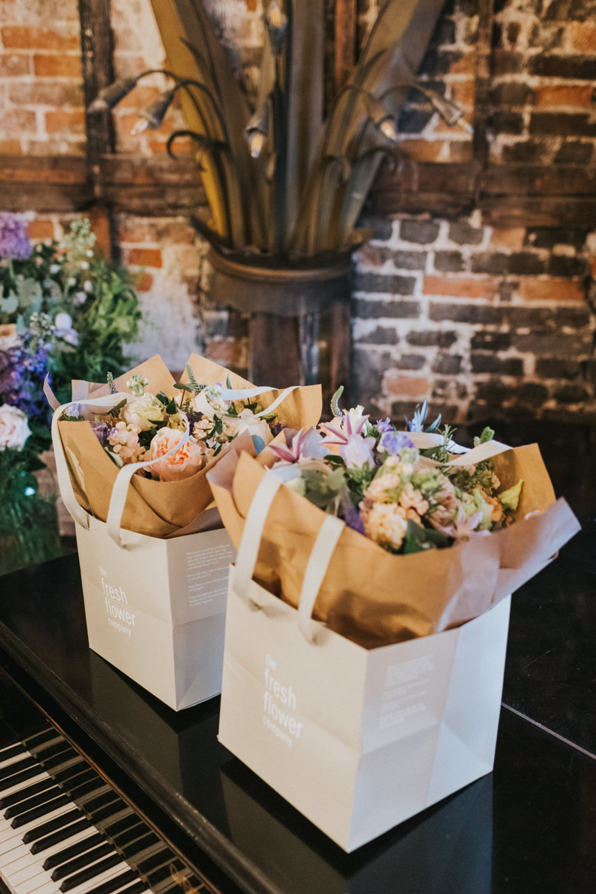 Two floral arrangements in "The Fresh Flower Company" bags sit on a piano at Brunswick House. Brick and timber frame walls add character to this wedding venue.