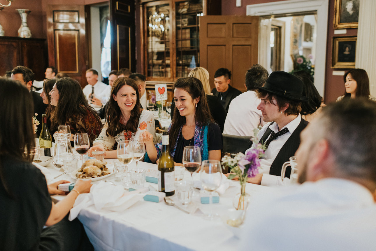 Guests enjoying a Brunswick House Wedding reception, seated at a long table with wine, flowers, and smiles in an elegant, historic setting.
