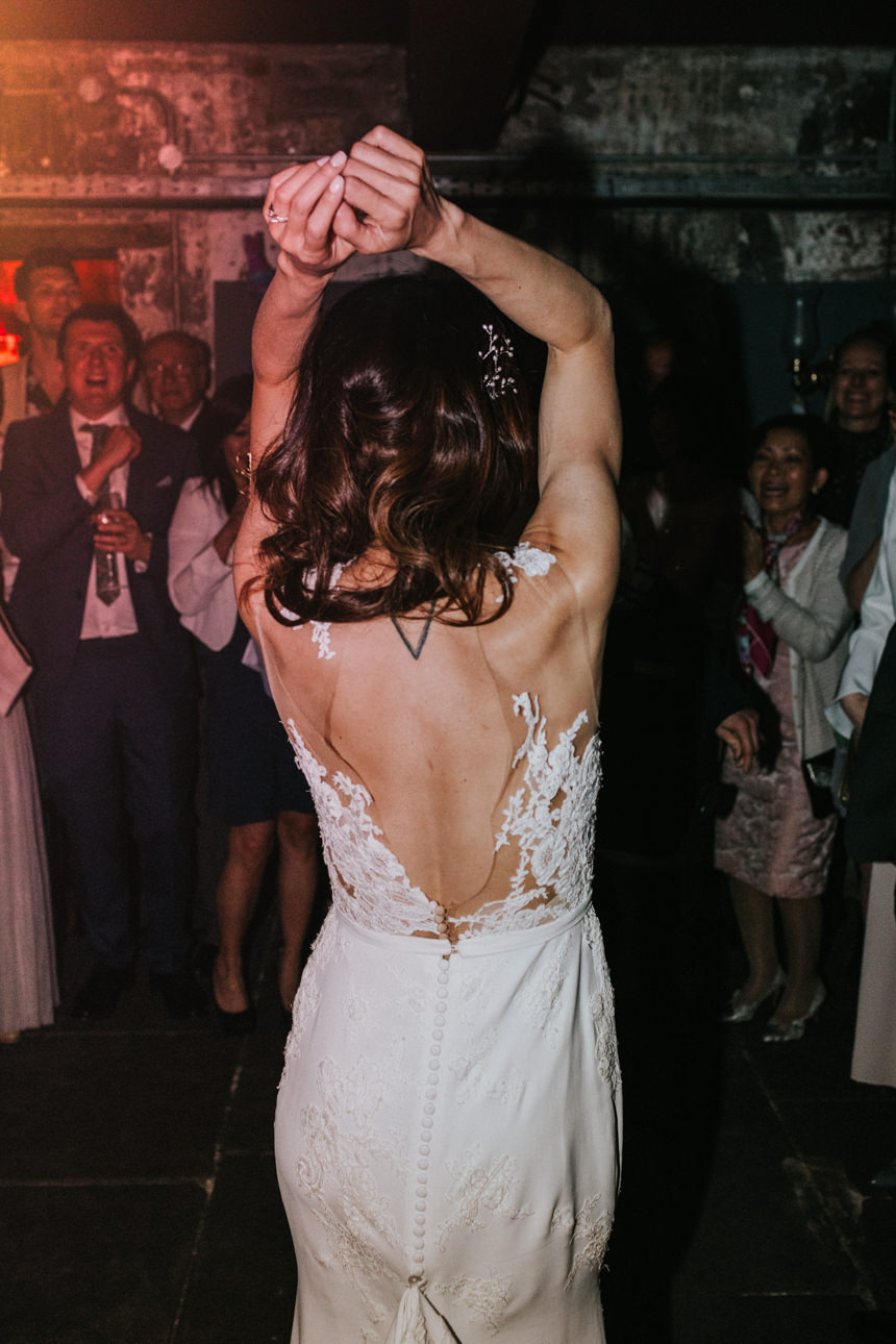 Brunswick House wedding: Bride in a lace-backed gown dances with arms raised at her reception. Guests watch, enjoying the celebration.